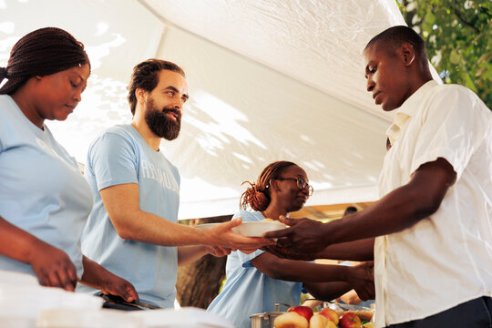Interracial group in support of hunger relief volunteering in distribution of essential items and free food to needy and less fortunate individuals. Poor and homeless people receive humanitarian aid.