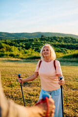 Obraz premium Happy senior woman with trekking poles enjoying Nordic walking activity in nature, staying active and healthy in retirement