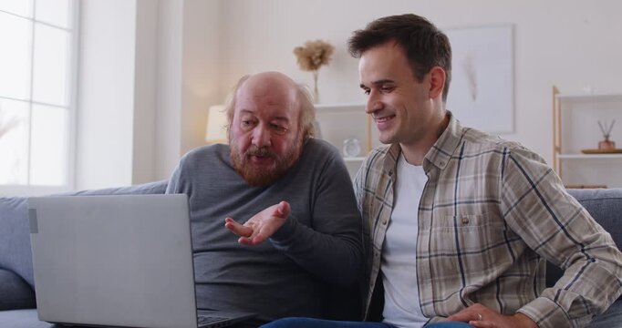 Helping senior with laptop, grown-up son, grandson and old father learning how to use computer, choose goods or services via internet or web surfing together at home, new useful apps, on-line services