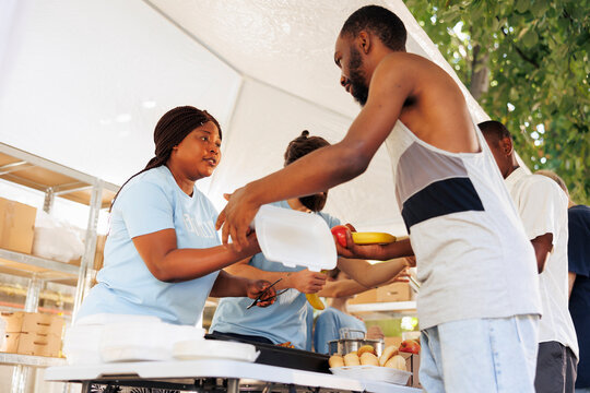 Young black woman helping the needy through food donation and volunteering in a community outreach program. Charity workers at food drive share fresh produce and necessities to poor, homeless people.