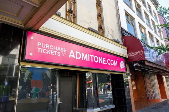 A bright pink Purchase Tickets at Admitone.com sign above a black-tiled box office entrance, next to the neon Roxy cabaret sign on Granville Street.