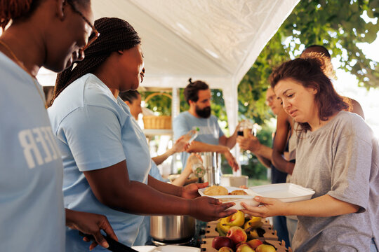 Hunger relief team of volunteers donates essential items and free food to needy, showing generosity in serving less fortunate. Non-profit outdoor food bank sharing warm meals to poor homeless people.