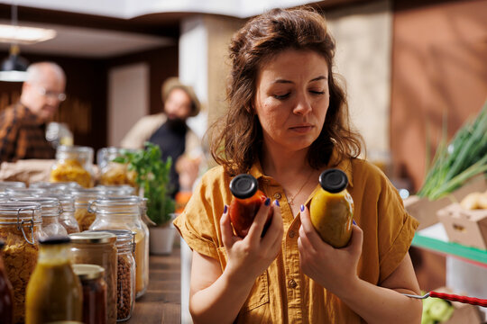 Green living woman in zero waste store interested in purchasing chemicals free products with high nutritional value while client does food shopping in sustainable local neighborhood shop.