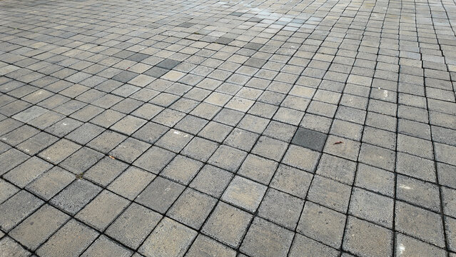 An expansive surface of interlocking stone pavers arranged in a geometric pattern showcasing varying shades of grey with mossy textures.