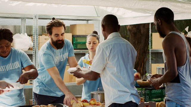 At community center young and pleasant group of volunteers serving warm food and helping the needy, charity workers providing hunger relief to the underprivileged and homeless people.