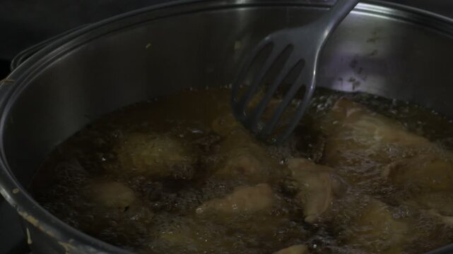 samosas being deep fried in hot oil inside a pan, with a slotted spatula used during the cooking process. the image captures the preparation of a popular crispy snack in a kitchen setting