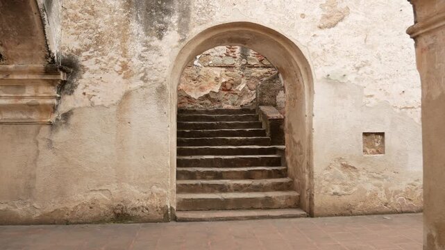 A straight-on view of a sturdy, old stone staircase descending through a rough-hewn arched opening. The staircase disappears upwards into darkness.  