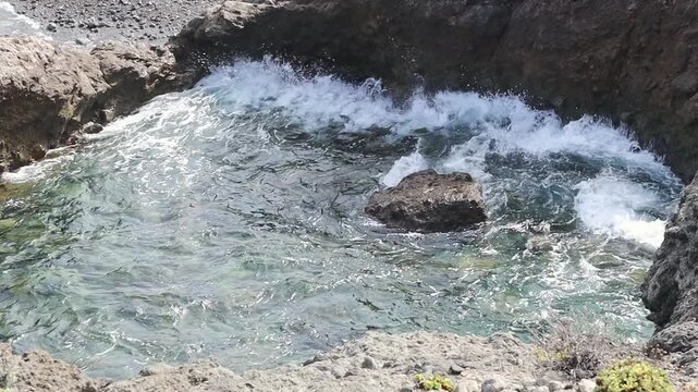 Picturesque view of the natural volcanic pool Charco del Viento with violently splashing water crashing against the rocks in the Atlantic Ocean on an autumn day, viewed from the side, close-up with sl