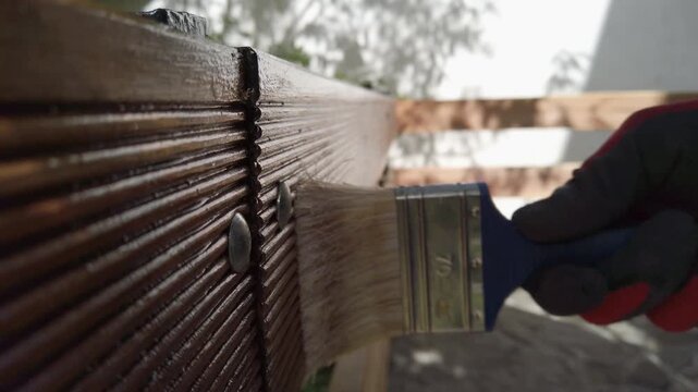 Hand in glove painting fence of impregnated ship floor planks. Carpenter applying protective layer of varnish.