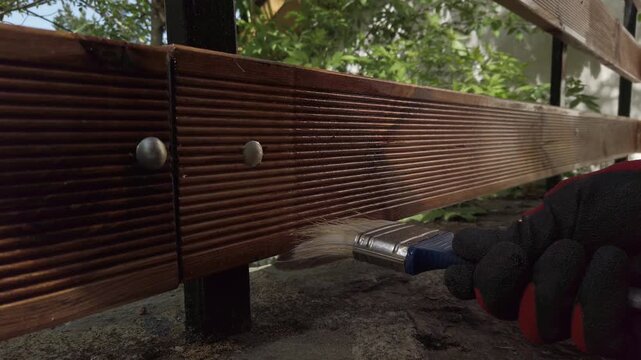 Hand in glove painting fence of impregnated ship floor planks. Carpenter applying protective layer of varnish.