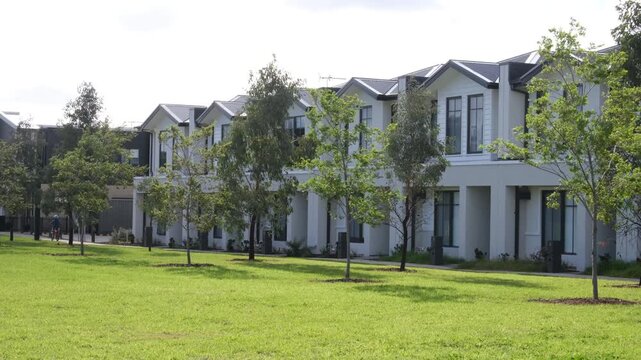 A row of modern two-storey townhouses facing a green parkland reserve in a new residential estate,Truganina, Melbourne, Australia. A child rides a bicycle along a footpath in the distance