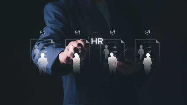Businessman holding a magnifying glass with HR text over virtual resume profiles of candidates with checkmarks, Concept of human resources, recruitment, talent acquisition, and candidate screening.