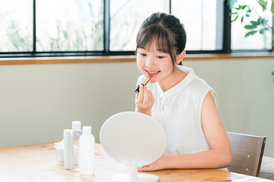 A child, a girl, elementary school or middle school age, applying lipstick and makeup while looking in the mirror.
