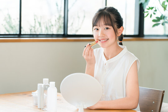 A child, a girl, elementary school or middle school age, applying lipstick and makeup while looking in the mirror.