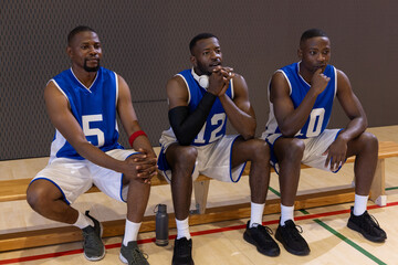 Fototapeta premium African American male teammates in blue jerseys sitting on bench on court with bottle phones sleeve