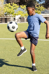 African American male child juggling soccer ball while wearing blue tshirt navy shorts on pitch © wavebreak3