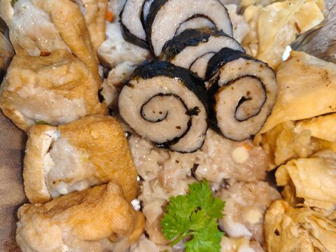 Assorted Indonesian dimsum and siomay with fried wontons and stuffed tofu served in an aluminum foil tray, garnished with fresh parsley. High angle view.