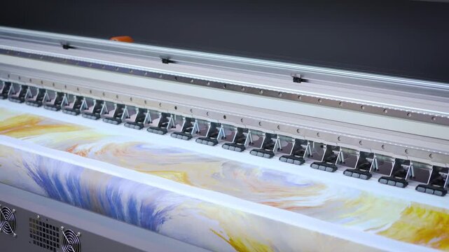 Large format printer in motion printing colorful abstract design on wide roll of fabric material in slow motion.