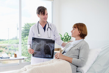 Obraz premium Doctor intently reviews detailed X-ray with patient lying comfortably in hospital bed; bright room showcases medical equipment and scenic window view for healthcare consultation.