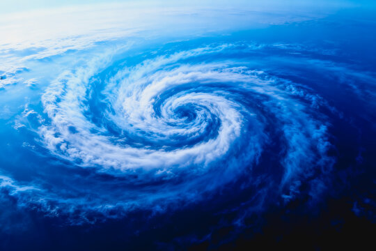 A high-angle aerial shot of a large rotating tropical cyclone with distinct spiral cloud bands over deep blue ocean waters.