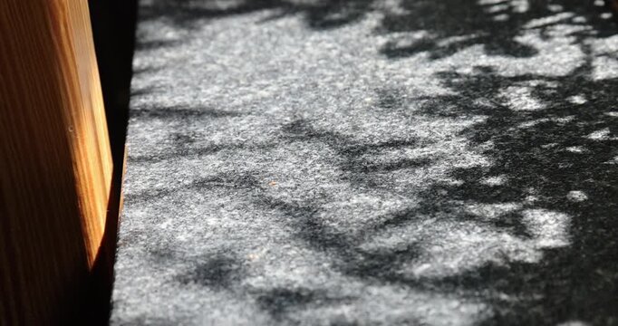 Close-up of the light and shadow on the wooden window sill, the dappled shadows of trees, and the texture of the stone tabletop.