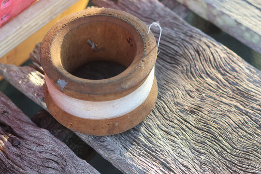A close-up high-angle commercial view of an authentic weathered wooden handline fishing reel wrapped with nylon monofilament line and a metal hook resting on rustic textured timber