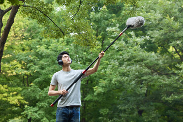Young man recording natural sounds outdoors with boom microphone in green park © HaXuanDieu
