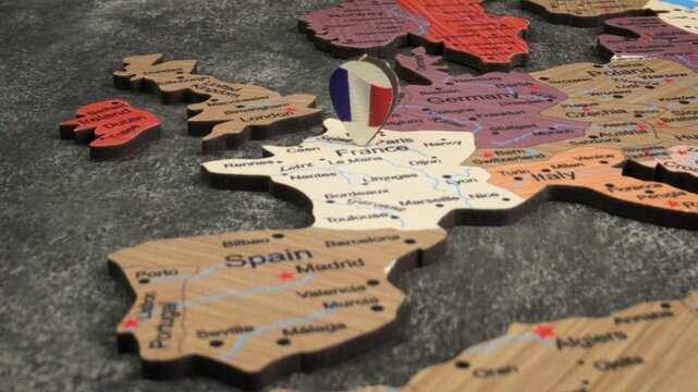 A close up video of a France flag map pin on a wooden map of Europe, showing other European countries like Spain, UK, Germany, and Italy.