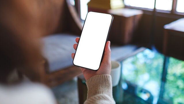 Mockup image of a woman holding and using mobile phone with blank desktop screen in cafe
