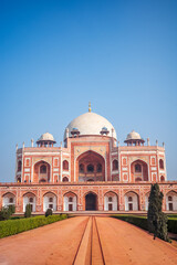 Obraz premium Vertical composition of Humayun’s Tomb in New Delhi, India, featuring its iconic white marble dome, red sandstone facade, symmetrical Mughal architecture, and landscaped gardens beneath a sky