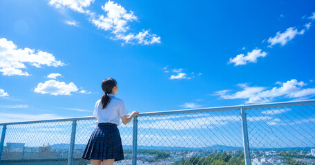 Naklejka premium 屋上フェンスから青空を見上げる女子高校生の後ろ姿