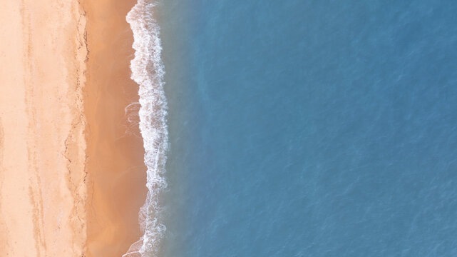 Aerial drone view of turquoise ocean waves washing onto a sandy tropical coastline. Minimal beach background with generous copy space, ideal for travel advertising, summer campaigns, tourism branding,