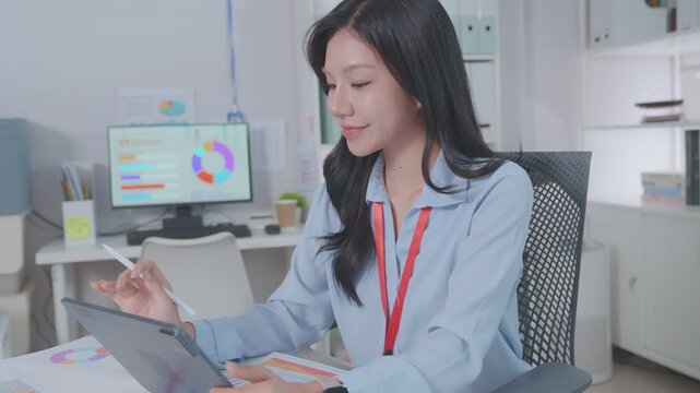 Smiling asian business woman using tablet laptop with equipment placed for doing finance on an home office desk, tax, report, accounting, statistics, and analytical research concept.
