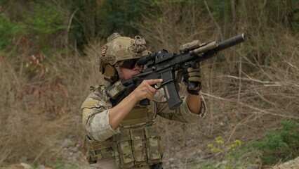 Fototapeta premium A special forces soldier in full combat gear advances during a tactical mission, aiming his assault rifle while patrolling a rugged, hostile environment.