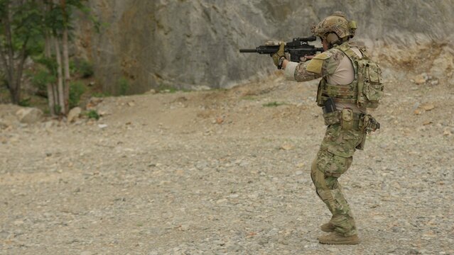A special forces soldier aims his assault rifle during a tactical training exercise in a rocky, outdoor environment, practicing marksmanship and combat readiness.