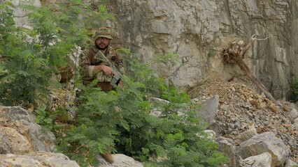 Obraz premium A soldier in full tactical gear patrols a rugged mountain area, conducting surveillance and maintaining security during a special operations reconnaissance mission.