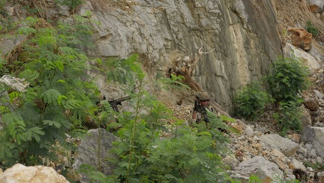 Camouflaged special forces soldiers conduct a covert surveillance mission, securing a tactical position among rugged rocks in a hostile environment.