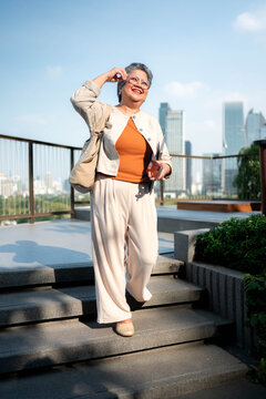 Confident senior woman standing outdoors with a tablet in a modern city setting