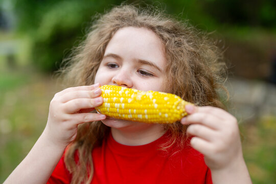 Child holding corn with cute face. Child portrait captures adorable summer lifestyle. Curly girl enjoys child snack outdoors. Healthy food gives child enjoyment.