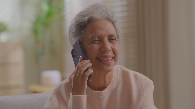 Smiling older woman talking mobile phone call conversation at home on sofa retired lady grandmother senior female talk smartphone receiving family sit on sofa at home.