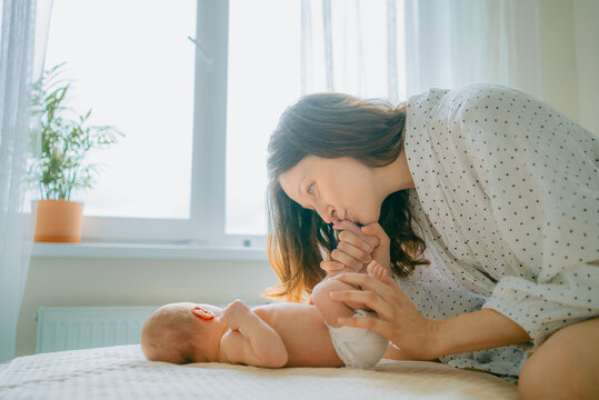 Mother bonding with her infant child in a sunlit bedroom, showing affection and devotion by kissing the baby's foot, representing family and new life