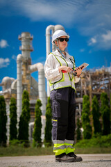 Engineer inspector refinery hard hat safety vest tablet industry worker stands outdoors at petrochemical plant, checking digital checklist, focusing on safety compliance under blue sky © ADD PHOTO