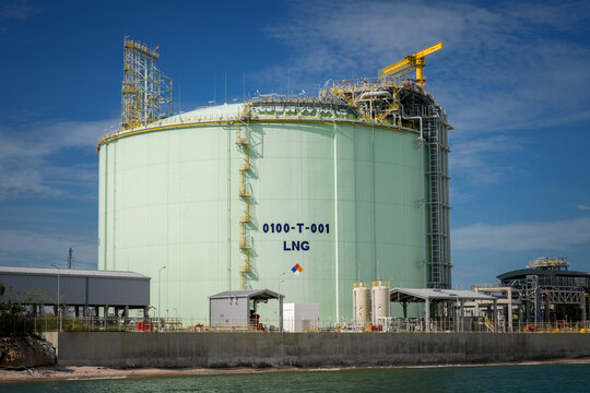 Liquefied natural gas storage tank energy industry terminal refinery gas fuel, large cryogenic vessel at coastal port facility with ladder and crane under blue sky, industrial safety mood