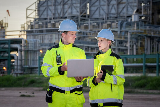 Industrial worker engineer safety helmet high visibility jacket refinery laptop team meeting at chemical plant, discussing inspection checklist with tablet, focused professional mood