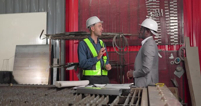 Sales engineer and client confirm a business agreement in an industrial workshop, shaking hands and reviewing contract documents for a custom manufacturing project.
