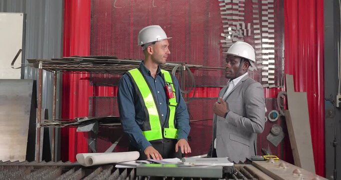 Sales engineer and client confirm a business agreement in an industrial workshop, shaking hands and reviewing contract documents for a custom manufacturing project.
