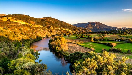 Obraz premium A serene river meanders through a picturesque valley surrounded by lush greenery and rolling hills under a clear blue sky