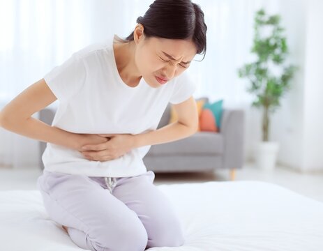 Woman Experiencing Stomach Pain, Clutching Abdomen, Suffering Discomfort Indoors.