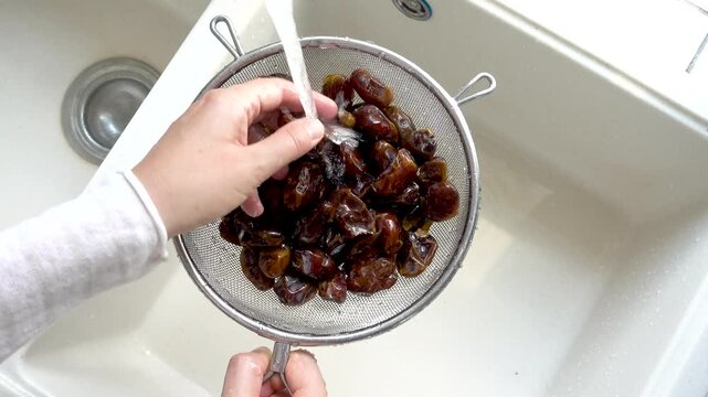 Female hands wash dried dates in a mesh strainer under running water in a kitchen sink. Concept of healthy eating and using natural sweeteners. Ideal for nutrition, vegan diet, and cooking content