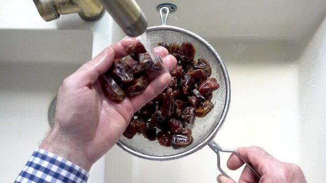 Male hands wash dried dates in a mesh strainer under running water in a kitchen sink. Concept of healthy eating and using natural sweeteners. Top view. Ideal for nutrition, vegan diet, cooking content